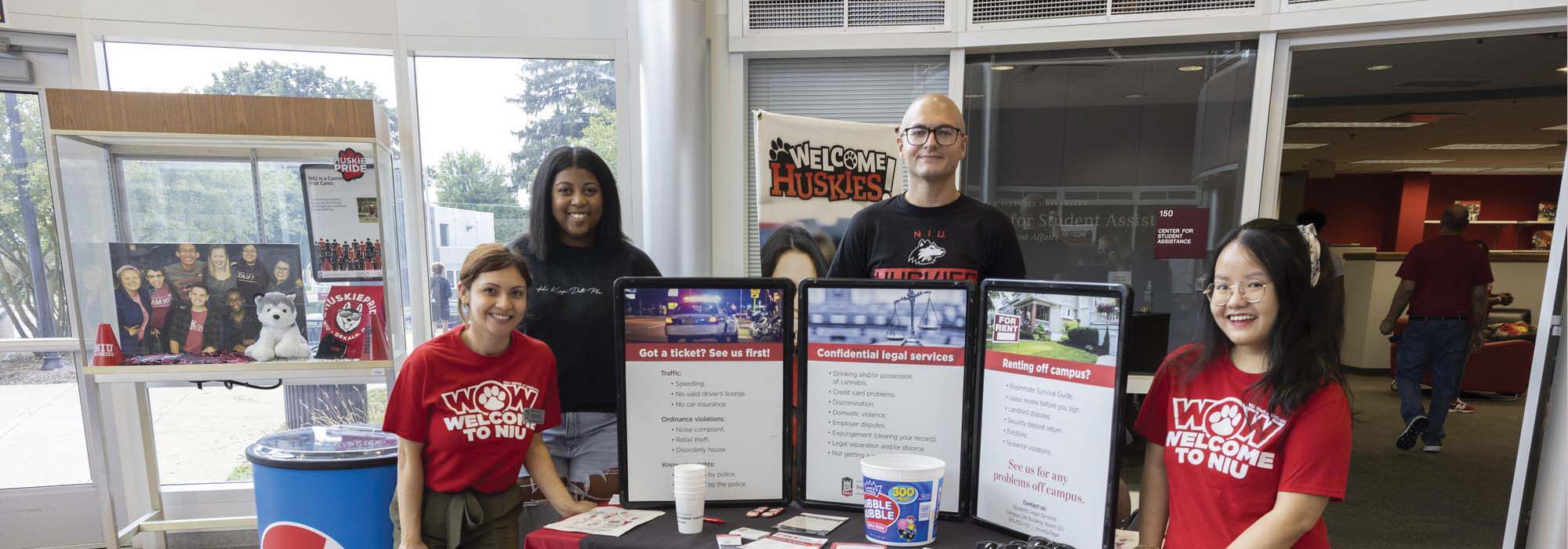 Smiling staff and students at an information table in the campus life building
