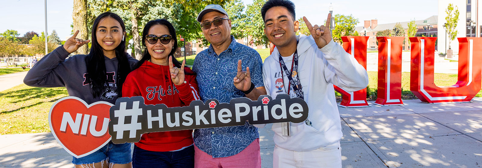 Student with family standing outside in MLK Commons near Huskie Pride sculpture